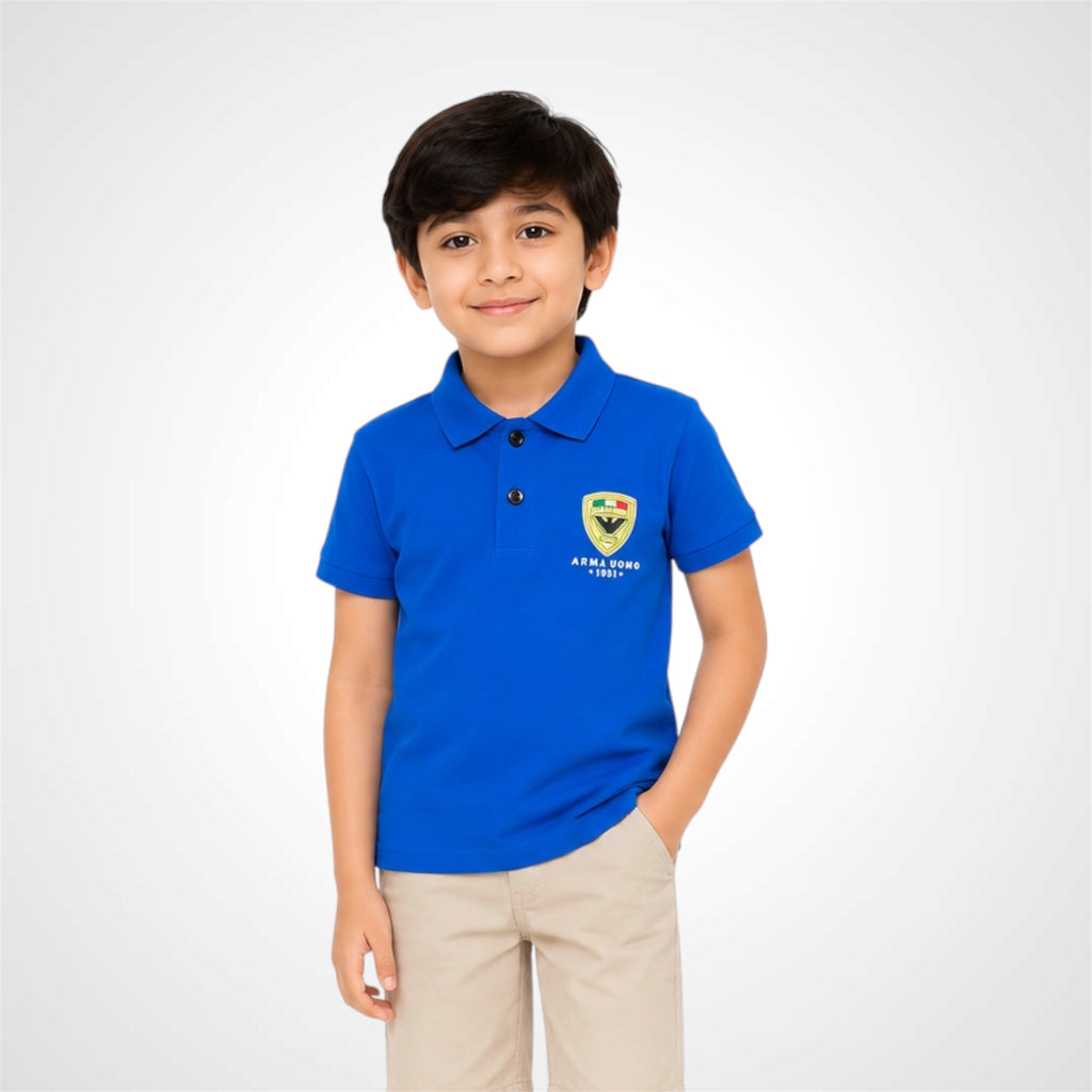 A young boy wearing a bright blue polo shirt with a school crest on the left chest and khaki trousers, standing against a light gray studio background.
