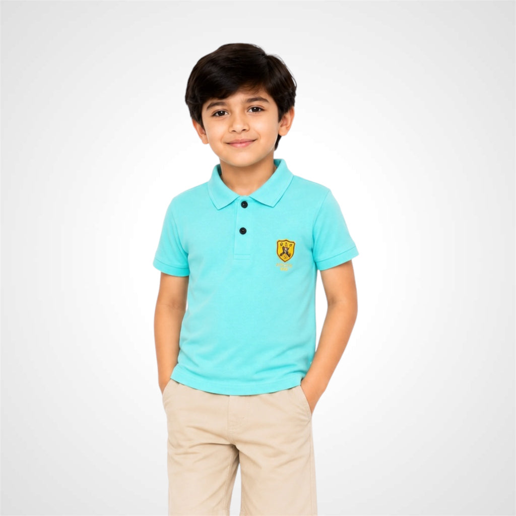 A young boy wearing a light turquoise polo shirt with a small yellow and black shield logo on the left chest, paired with beige trousers, standing against a light gray studio background.