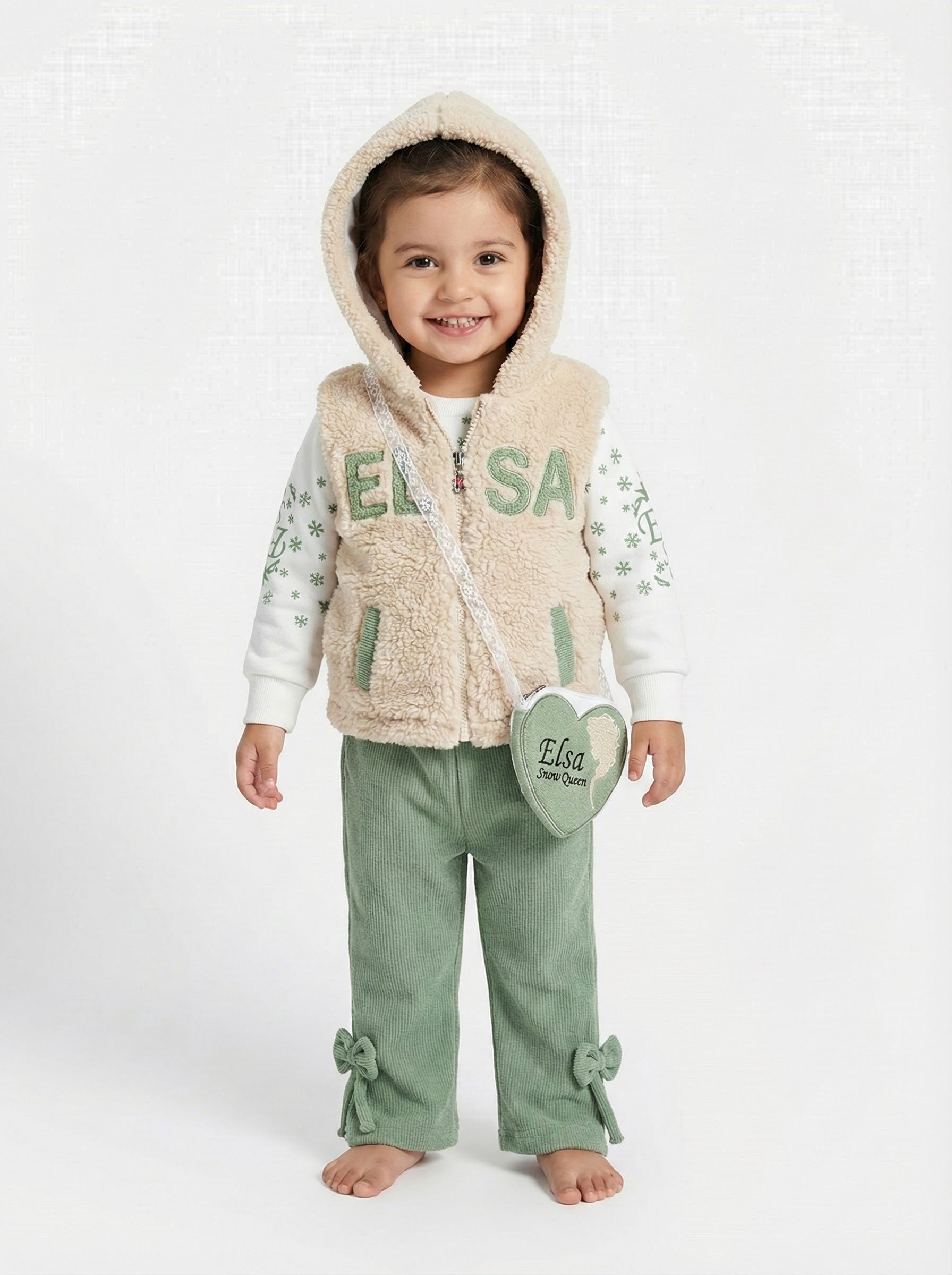 Young girl wearing a beige hooded 'Elsa' fleece vest, patterned top, and orange corduroy trousers with cute bow details at the hem green