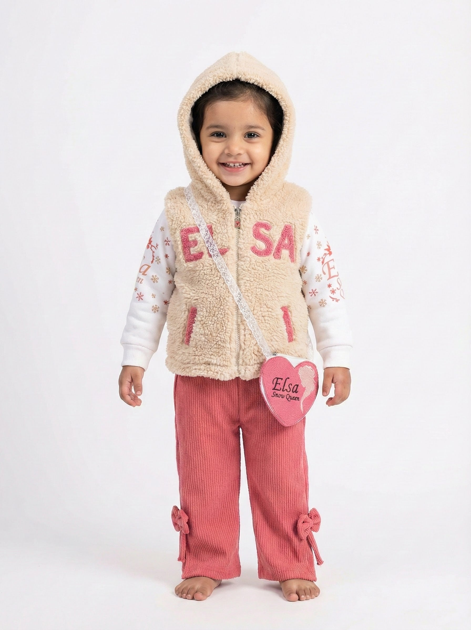 Young girl wearing a beige hooded 'Elsa' fleece vest, patterned top, and orange corduroy trousers with cute bow details at the hem pink