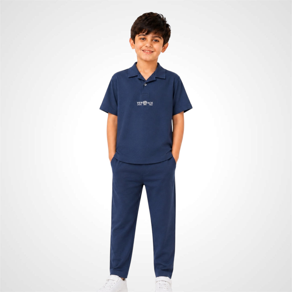 A young boy modeling a navy blue short-sleeve polo shirt and matching navy blue pants, standing against a light gray studio background.